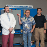 Allison Bertl, Nathan Origer, Thomas Box, Chad Huber and Andrew Pesaresi stand in front of an electrical wiring training system in the training room at Winamac Coil Spring.