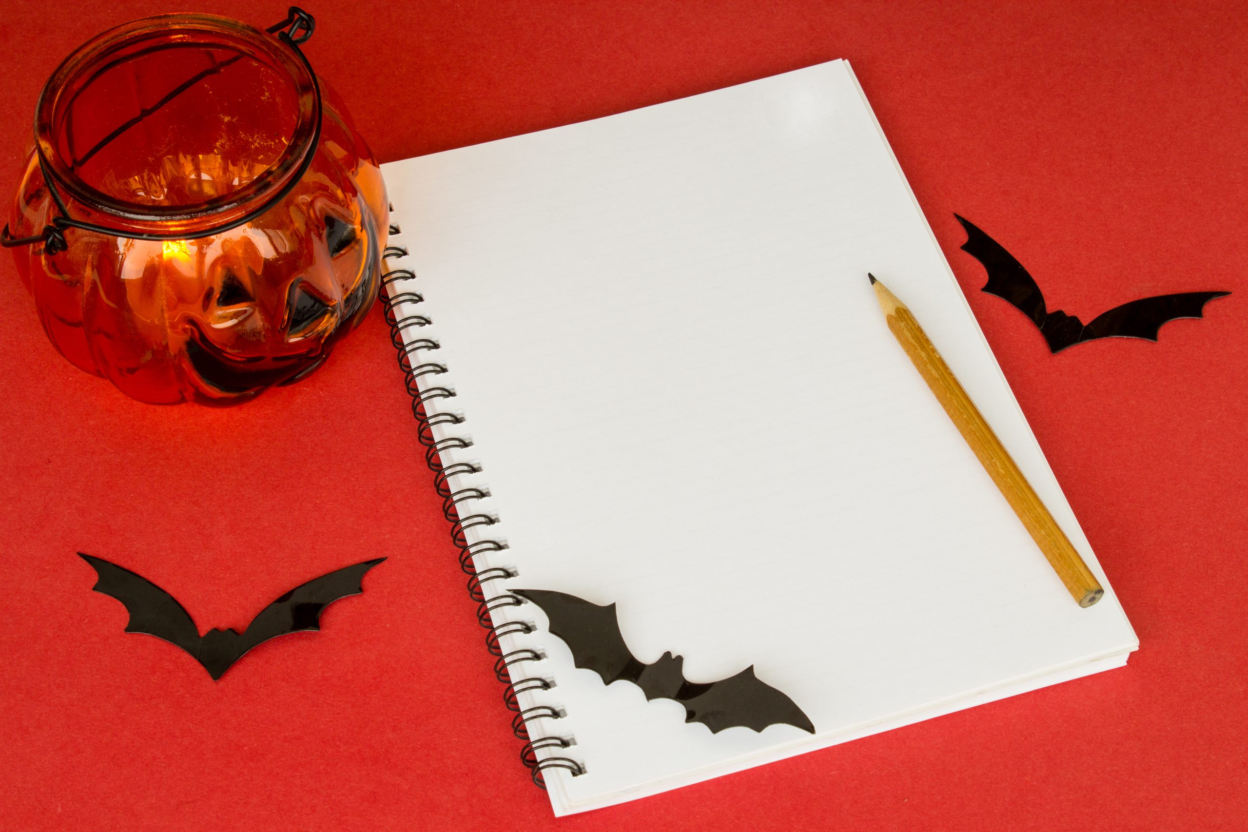 Halloween notepad. Pumpkin lantern, pen, bats and notepad on a red background. Traditional halloween decor concept. Copy space. Flatlay. Top view.