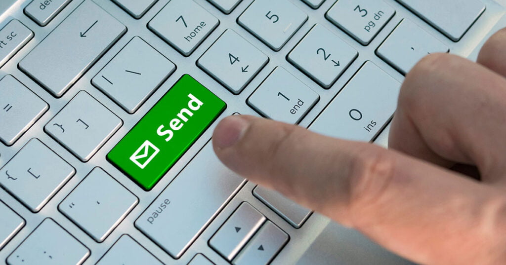 Email send button on the computer keyboard. A male finger presses a color button on a gray silver keyboard of a modern laptop. Button with inscription close up.